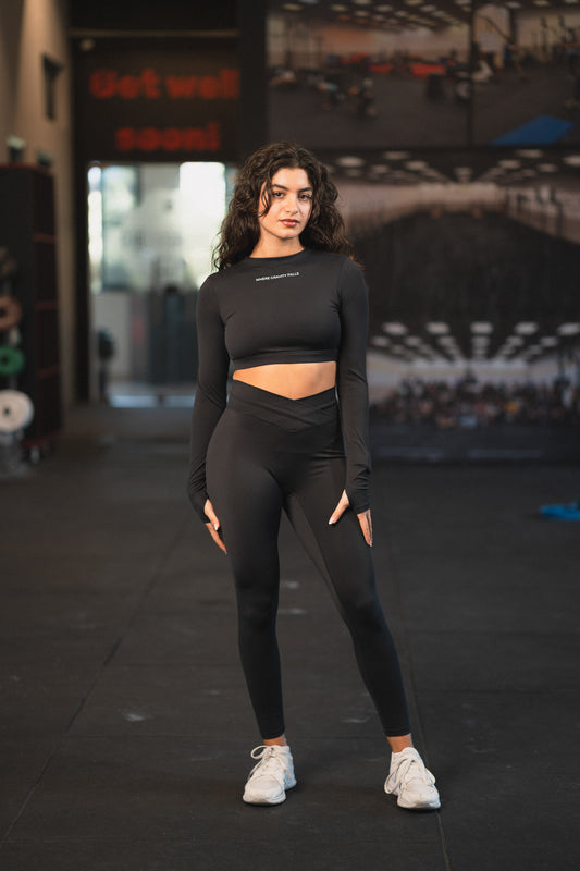 Front view of the Where Gravity Falls Eclipse black cropped long sleeve top with small chest logo, worn with black leggings